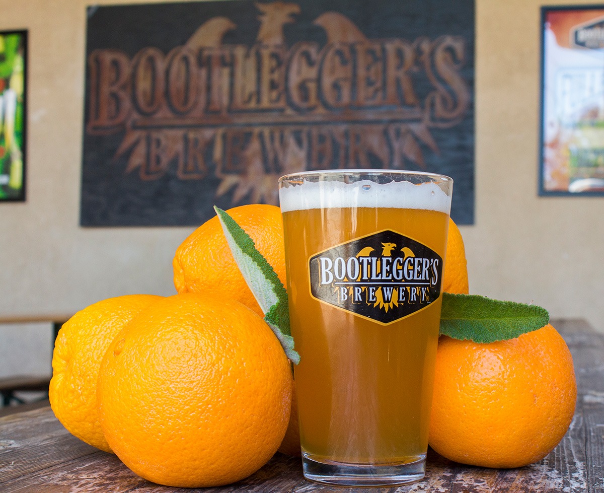 Hazy beer surrounded by oranges with Bootleggers logo in back